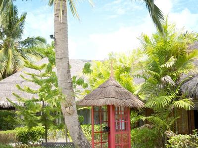 Tropischer Garten mit Palmen, grünen Büschen und kleinen Hütten mit Strohdächern.