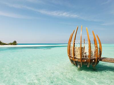 Klare türkisfarbene Lagune mit hölzernem, tropischem Pavillon und blauem Himmel im Hintergrund.