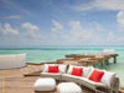 Holzsteg mit weißem Lounge-Sofa, roten Kissen und türkisfarbenem Meer unter blauem Himmel.