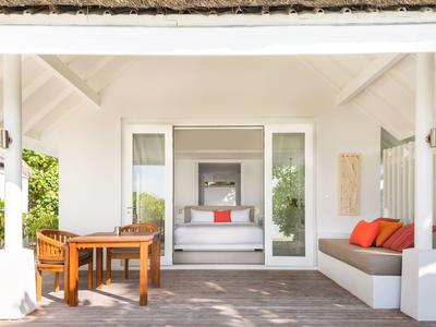 Helle Terrasse mit Holztisch, Sofa mit orangen Kissen und Blick ins Wohnzimmer mit weißem Sofa.