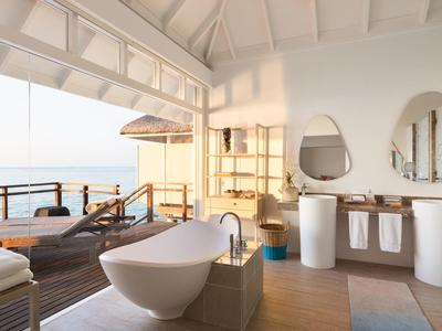 Geräumiges Badezimmer mit freistehender Badewanne, Holzfußboden und offener Terrasse mit Meerblick.