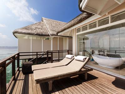 Sonnenterrasse mit zwei Liegestühlen, Holzboden und Blick aufs Meer bei bewölktem Himmel.