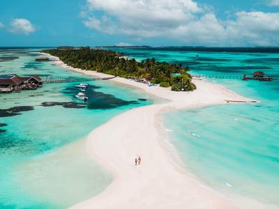 Weißer Sandstrand mit türkisblauem Wasser und grünen Palmen unter blauem Himmel und Wolken.