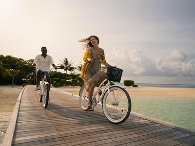 Deux personnes font du vélo sur une jetée au bord de la mer sous un ciel nuageux.