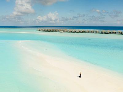 Plage avec eau turquoise et une personne marchant sur le sable.