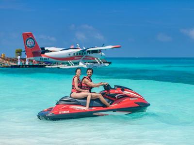 Deux personnes assises sur un jet ski rouge dans une eau turquoise claire sous un ciel lumineux.
