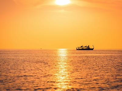 Bateau sur une mer calme au coucher du soleil avec ciel orange.
