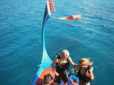 Trois plongeurs sur un bateau se préparent pour une plongée dans une mer bleue claire.