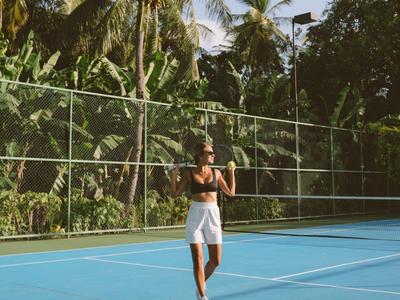 Femme en tenue de sport sur un court de tennis entouré de palmiers.