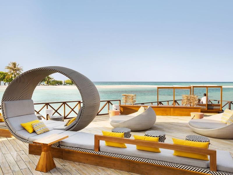 Moderner Outdoor-Loungebereich mit runden Sitzmöbeln, Holzboden und Blick aufs blaue Meer.