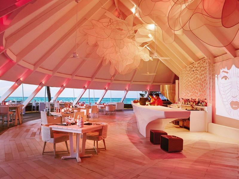 Modernes Restaurant mit vielen runden Holztischen, Stühlen und barhockerförmiger Sitzbank in warmem Licht.