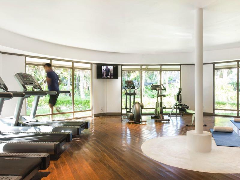 Moderner, heller Fitnessraum mit Holzfußboden, großen Fenstern, Laufbändern und Trainingsgeräten.