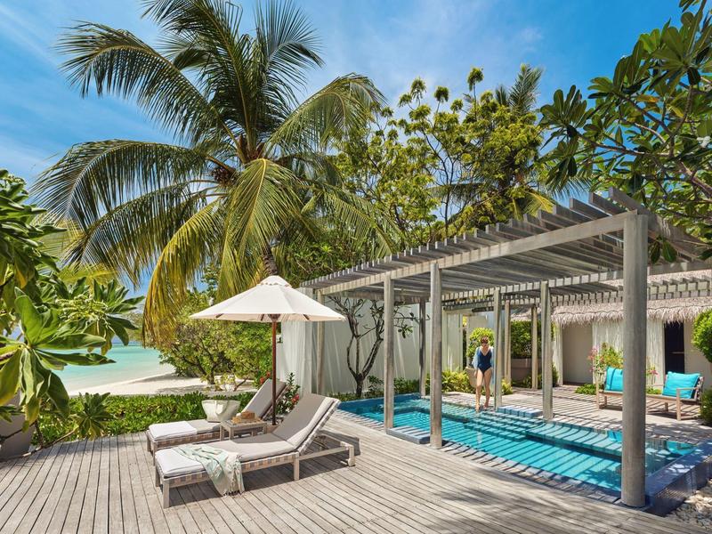 Strandbereich mit zwei Liegen, Sonnenschirm, Palmen und überdachtem Sitzbereich am Meer.