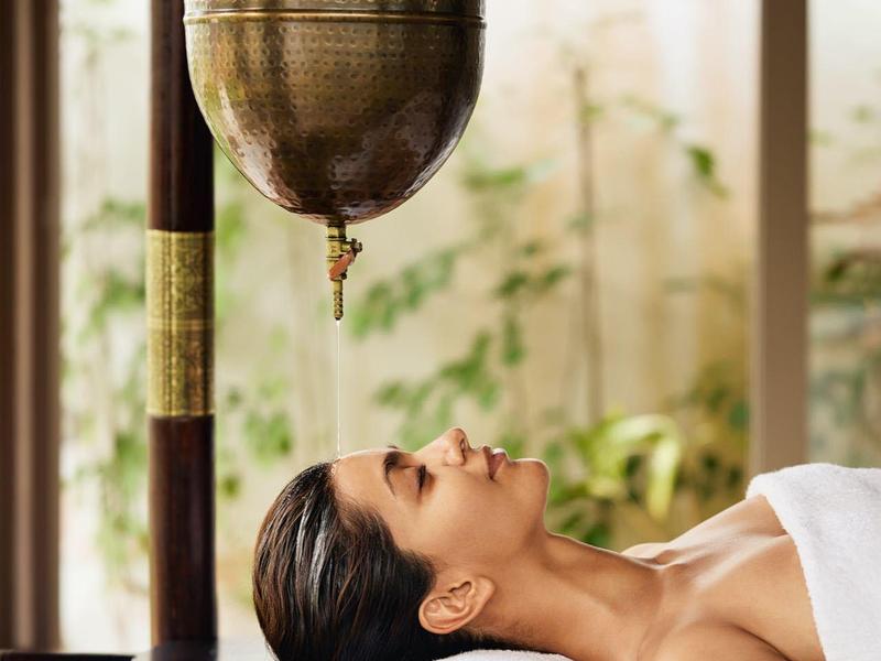 Frau liegt entspannt mit geschlossenen Augen unter hängendem Kupfergefäß in ruhigem Raum.