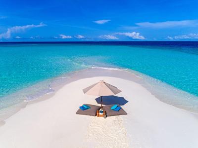 Ein Paar entspannt unter einem Sonnenschirm auf einem Sandstreifen im klaren blauen Meer.