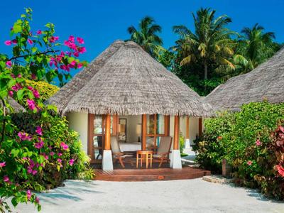 Strandbungalow mit Strohdach, umgeben von tropischen Pflanzen und weißem Sand.