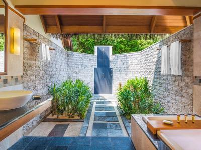 Freiluftbad mit Badewanne und Waschbecken, umgeben von Steinmauern und Pflanzen.