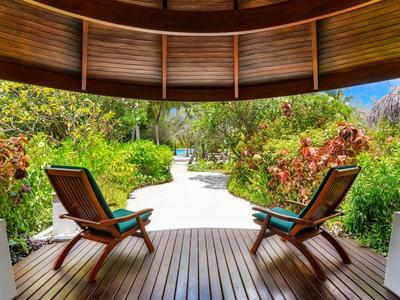 Holzterrasse mit zwei Stühlen und Blick auf einen Weg durch üppige Vegetation.