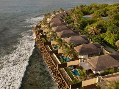 Alignement de villas avec piscines au bord de la mer entourées de verdure.