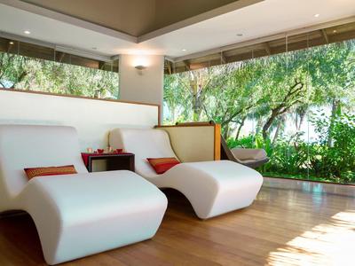 Moderne Lounge mit weißen Sessel und großen Fenstern, Blick auf einen grünen Garten.