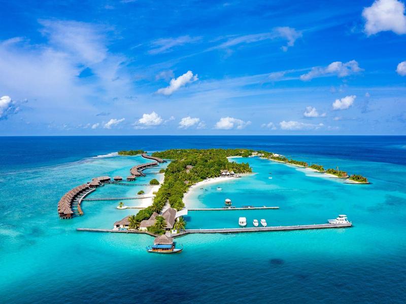 Luftaufnahme einer tropischen Insel mit umgebendem türkisfarbenem Wasser und blauem Himmel.
