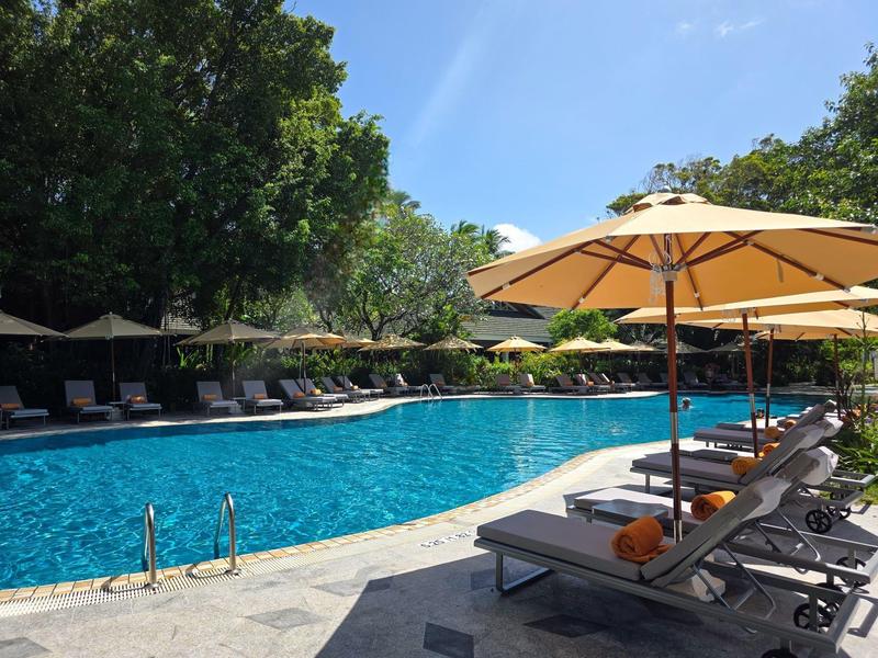 Großer Außenpool mit Liegestühlen und Sonnenschirmen in einem Hotelgarten.