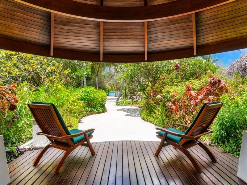 Holzterrasse mit zwei Stühlen und Blick auf einen Weg durch üppige Vegetation.