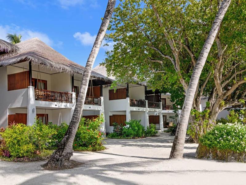 Strandhotel mit Strohdächern und Palmen an einem sonnigen Tag