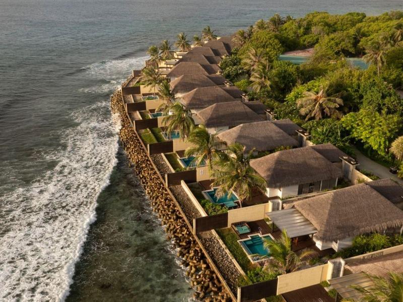 Reihe von Luxusvillen mit Pools am Meer, umgeben von grüner Vegetation.