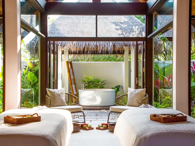 Gemütlicher Wellnessbereich mit zwei Behandlungsbetten und Blick auf einen Garten