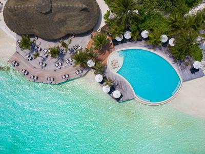 Luftaufnahme eines Hotels mit Pool, Sonnenliegen und Strand an türkisfarbenem Meer.