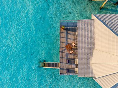 Holzsteg mit Terrasse über klarem, türkisfarbenem Wasser neben einem Wasserdachbungalow.