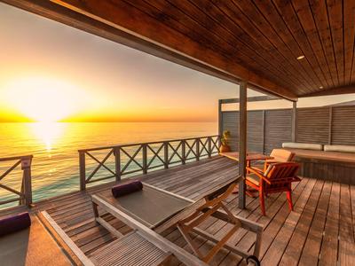 Holzterrasse mit Liegestühlen und einem Whirlpool bei Sonnenuntergang am Wasser.