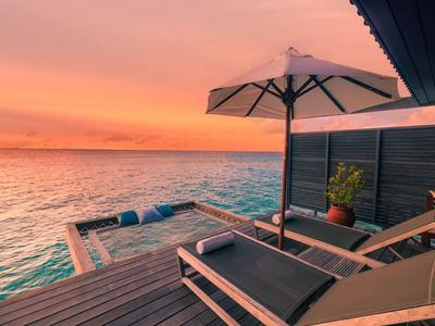 Eine Terrasse mit Sonnenliegen und Sonnenschirm mit Blick auf das Meer bei Sonnenuntergang.