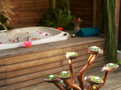 Holzverkleideter Whirlpool auf einer Terrasse mit grüner Dekoration und Kerzen.