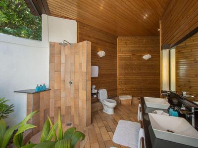 Moderner Außenbadbereich mit Holzverkleidung, Dusche, WC, Waschbecken und Sitzgelegenheiten in natürlicher Umgebung.