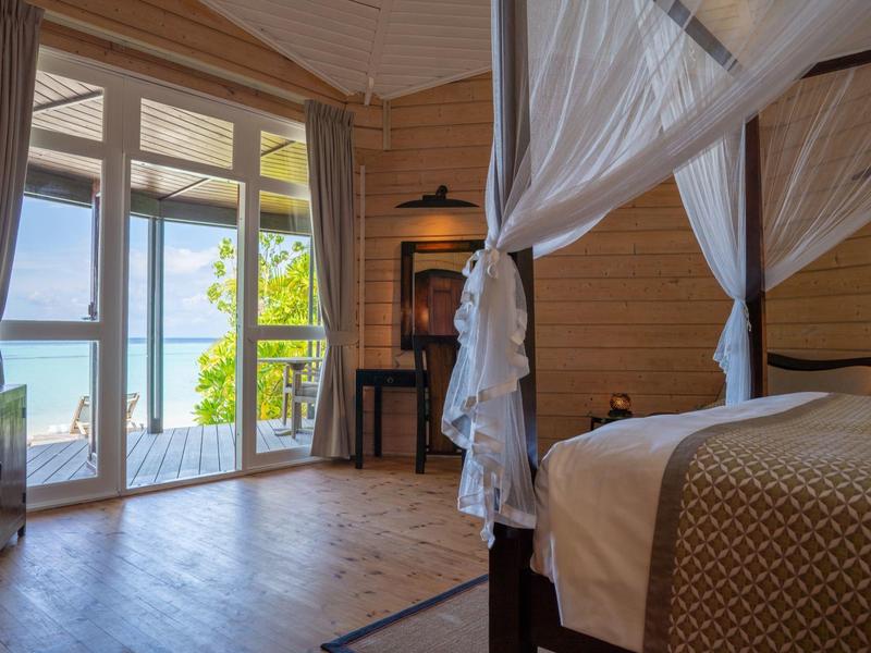 Gemütliches Zimmer mit Himmelbett und Blick auf das Meer durch große Fenster.