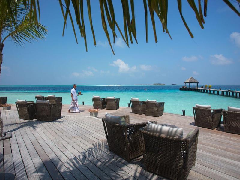 Loungebereich mit Sesseln auf einer Holzplattform am Strand mit Blick auf das türkisfarbene Meer.