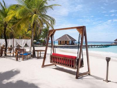 Plage avec feuilles de palmier, lit balançoire et chaises longues blanches sous des auvents près de la mer turquoise.