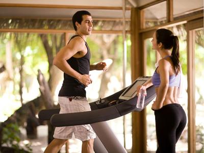 Un homme court sur un tapis roulant pendant qu'une femme le regarde dans une salle de sport d'hôtel moderne.