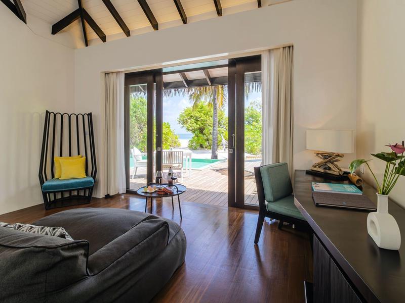 Helles Wohnzimmer mit dunklem Holzboden, Ledersessel, Schreibtisch, Pflanzen und Blick auf Terrasse.