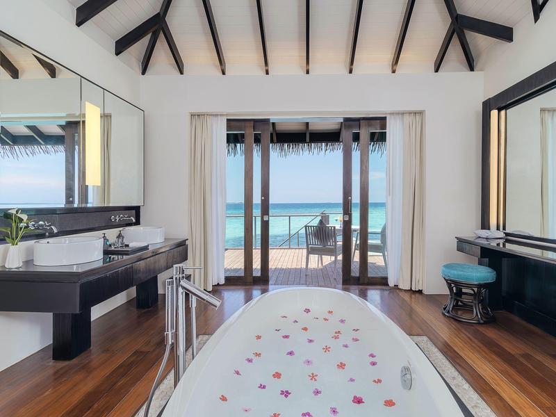 Helles Badezimmer mit freistehender Badewanne, Holzfußboden und Meerblick durch große Fenster.