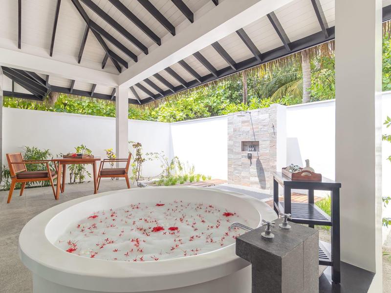 Weißes Badezimmer mit rundem Whirlpool, Blumenblättern im Wasser und Holzmöbeln in heller, offener Umgebung.