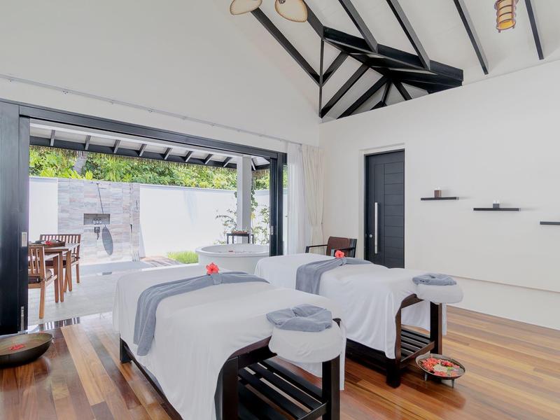 Moderne, helle Massageräume mit zwei weißen Betten und Holzfußboden, offene Glaswand zum Garten.