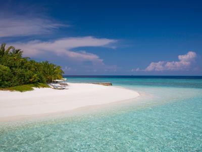 A tropical beach with white sand, clear turquoise water, and palm trees under a blue sky.