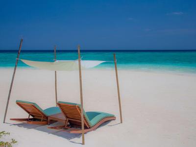 Two lounge chairs with a canopy on a white sandy beach by turquoise sea.