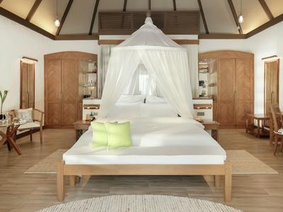 Helles Schlafzimmer mit Holzdecke, Baldachinbett und Holzmöbeln mit grünem Kissen.