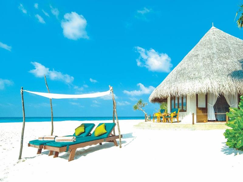 Strand mit Sonnenliegen und Hütte mit Strohdach unter blauem Himmel.