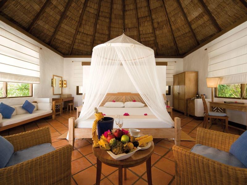 Gemütliches Hotelzimmer mit Himmelbett, Korbmöbeln und exotischer Früchteplatte.