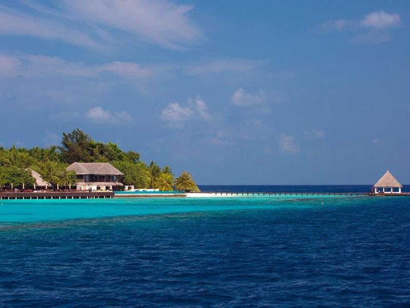 Blick auf eine tropische Insel mit Bungalows und türkisfarbenem Meer unter blauem Himmel.